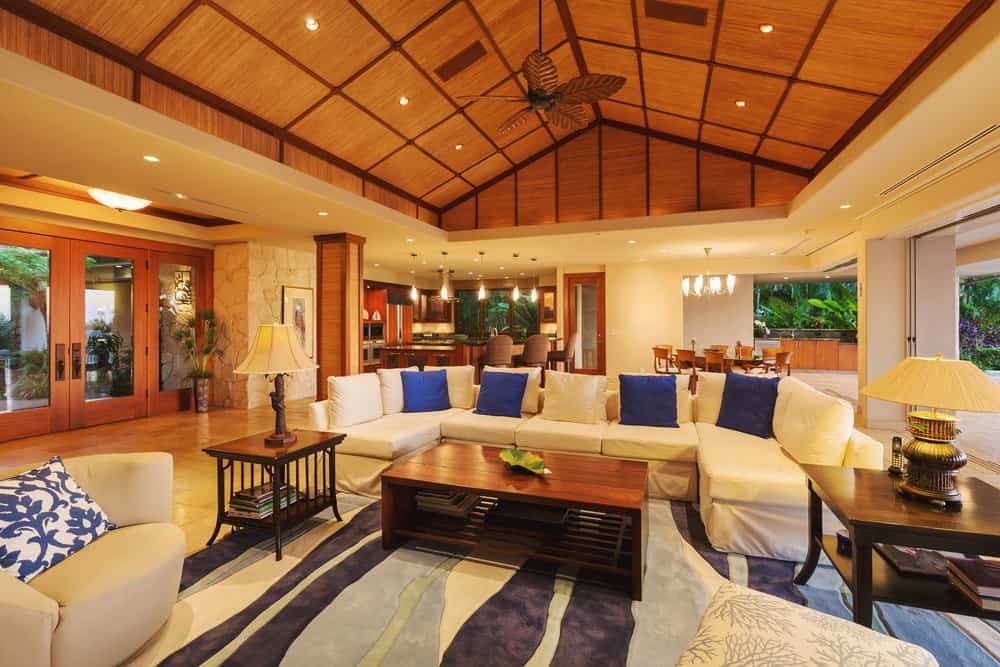 Phòng khách trần vòm gỗ với sofa kem gối xanh và cửa kính nhìn ra vườn