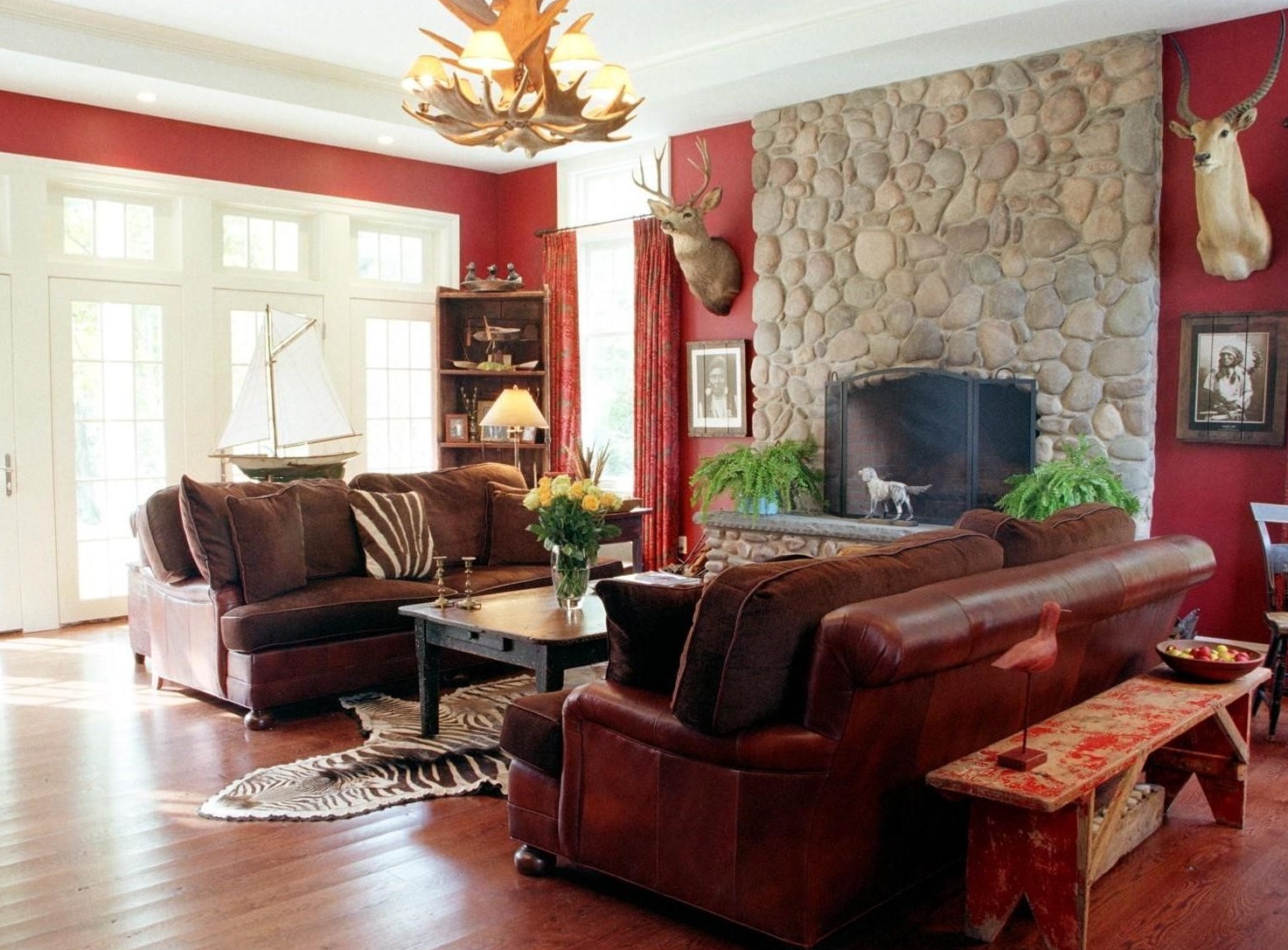 Phòng khách ấm cúng với sofa da nâu, lò sưởi đá, tường đỏ và đèn chùm sừng hươu.