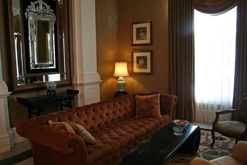 Phòng khách cổ điển với sofa nỉ nâu đỏ kiểu Chesterfield và gương khung vàng